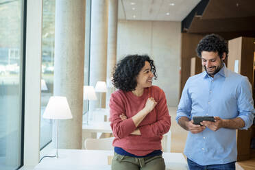 Happy man and woman discussing over tablet PC in library - JOSEF12578