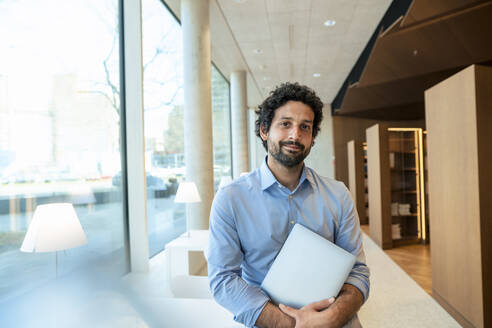 Lächelnder Professor mit Laptop in der Bibliothek - JOSEF12587