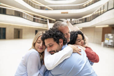 Senior businessman with eyes closed embracing colleagues in lobby - JOSEF12652