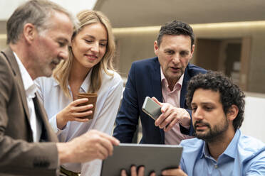 Lächelnde Geschäftskollegen, die im Büro über einen Tablet-PC ihre Strategie diskutieren - JOSEF12656