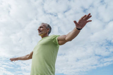 Mature man with arms outstretched under cloudy sky - VPIF07057