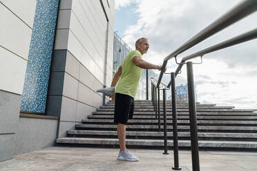 Man stretching leg standing by railing in city - VPIF07063