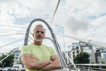 Selbstbewusster reifer Mann mit verschränkten Armen auf einer Brücke in der Stadt - VPIF07076