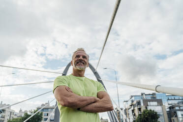 Smiling man with arms crossed standing on bridge in city - VPIF07078