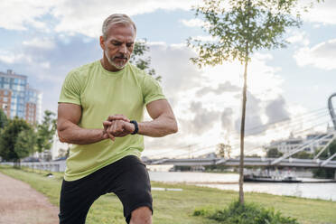 Mann überprüft Fitness-Tracker beim Stretching im Park - VPIF07092