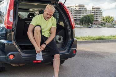 Mann bindet Schnürsenkel sitzend im Kofferraum eines Autos - VPIF07098
