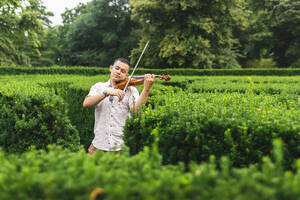 Geigerin übt Geige inmitten von Pflanzen im Park - DMMF00009