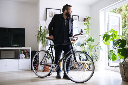 Geschäftsmann stehend mit Fahrrad im Wohnzimmer zu Hause - ASGF02714
