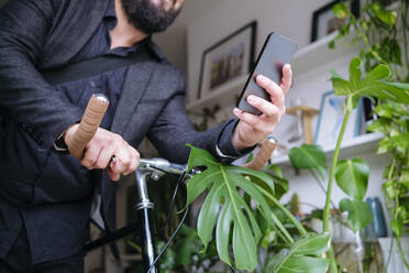 Freiberufler, der sein Smartphone benutzt und den Fahrradgriff bei Pflanzen zu Hause hält - ASGF02717