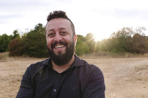Happy mature man with beard in field at sunset - ASGF02755