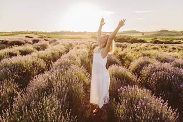 Frau stehend mit erhobenen Armen inmitten von Lavendelblüten im Feld - SIF00374