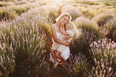 Smiling woman embracing daughter squatting in lavender field - SIF00376