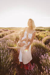 Frau stehend mit Töchtern in Lavendelfeld bei Sonnenuntergang - SIF00380