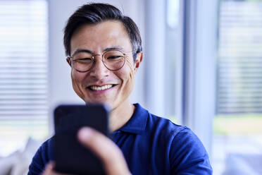 Glücklicher Mann mit Brille, der ein Selfie mit seinem Mobiltelefon macht - FMKF07702