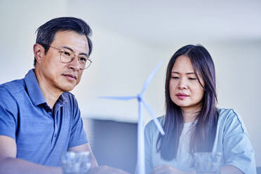 Mature man and woman examining wind turbine model at home - FMKF07728