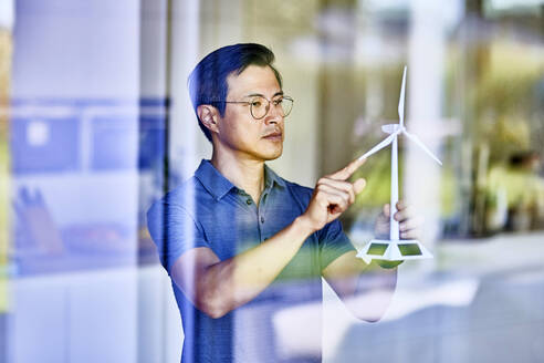 Mann begutachtet Modell einer Windkraftanlage durch Glas gesehen - FMKF07729