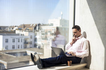 Mature businessman using laptop sitting in office - JOSEF12683