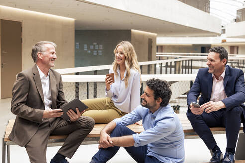 Happy business colleagues discussing strategy in office corridor - JOSEF12694