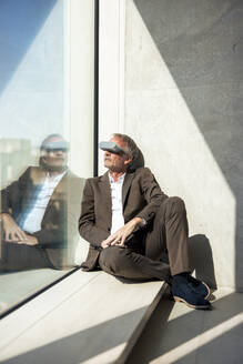 Älterer Geschäftsmann beobachtet durch eine intelligente Brille am Fenster im Büro - JOSEF12712