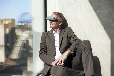 Senior businessman wearing VR glasses by window in office - JOSEF12715