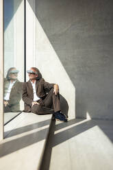 Smiling businessman wearing futuristic glasses by window in office - JOSEF12717