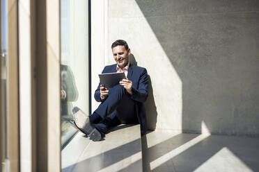 Lächelnder Geschäftsmann mit Tablet-PC im Büro sitzend - JOSEF12723