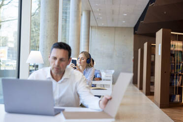 Älterer Professor arbeitet am Laptop am Schreibtisch in der Bibliothek - JOSEF12767