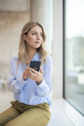 Nachdenkliche Geschäftsfrau mit Smartphone im Büro - JOSEF12787