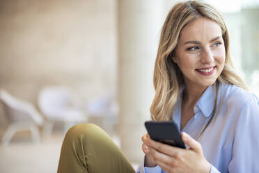 Smiling businesswoman with mobile phone in office - JOSEF12789