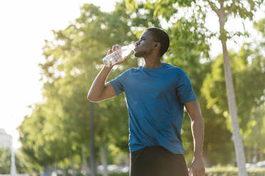 Junger Mann trinkt Wasser an einem sonnigen Tag - EGAF02520