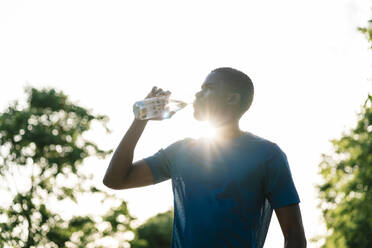 Junger Mann trinkt an einem sonnigen Tag Wasser aus einer Flasche - EGAF02521