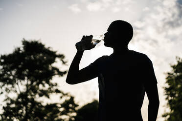 Junger Mann trinkt Wasser bei Sonnenuntergang - EGAF02522