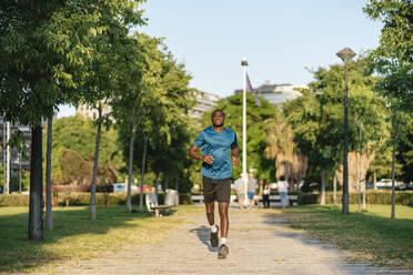 Junger Mann joggt im Park an einem sonnigen Tag - EGAF02534