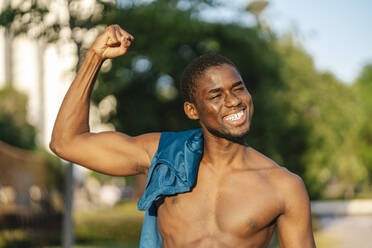 Glücklicher junger Mann beim Muskeltraining an einem sonnigen Tag - EGAF02536