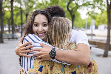 Glückliche junge Frau umarmt Freunde im Park - WPEF06273