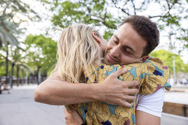 Smiling young man with eyes closed embracing girlfriend at park - WPEF06281