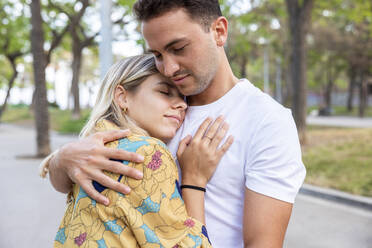 Boyfriend and girlfriend with eyes closed embracing each other at park - WPEF06289