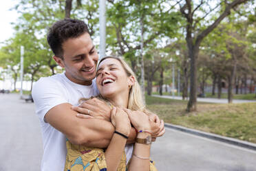 Happy man embracing cheerful girlfriend at park - WPEF06294