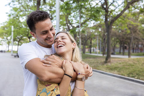 Glücklicher Mann umarmt fröhliche Freundin im Park - WPEF06294