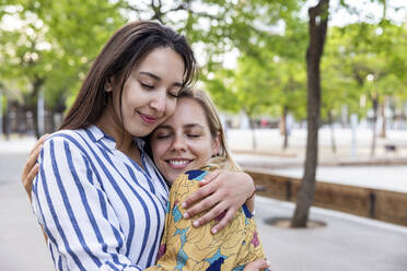 Lächelnde junge Frauen mit geschlossenen Augen, die sich im Park umarmen - WPEF06297