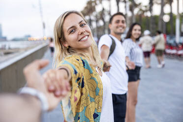 Smiling woman holding hands of friends enjoying at promenade - WPEF06312