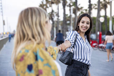 Glückliche Frau hält die Hände ihres Freundes an der Promenade - WPEF06313