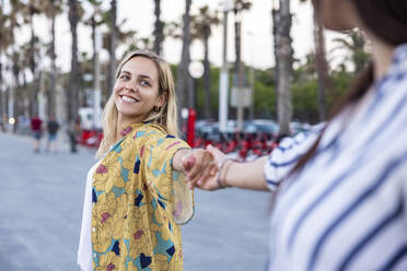 Lächelnde blonde Frau hält die Hand ihres Freundes an der Promenade - WPEF06314