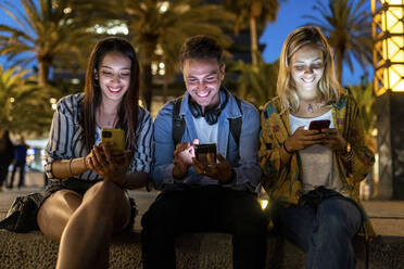 Glücklicher Mann und Frauen surfen nachts mit ihren Smartphones im Internet - WPEF06328