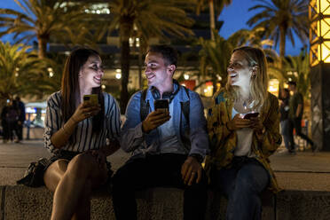 Happy friends holding smart phones talking with each other at night - WPEF06329