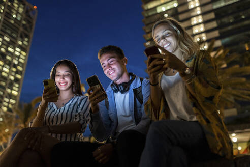 Glücklicher junger Mann und Frauen, die nachts mit ihren Smartphones im Internet surfen - WPEF06334