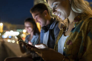 Lächelnde junge Frau, die ein Mobiltelefon benutzt und nachts bei Freunden sitzt - WPEF06335