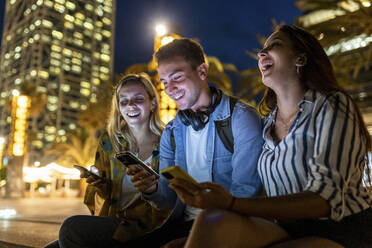 Fröhliche Frauen sitzen bei einem Freund und benutzen nachts ein Smartphone - WPEF06341