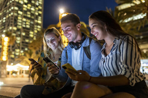 Glücklicher junger Mann, der nachts sein Smartphone mit Freunden teilt - WPEF06342