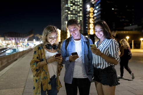 Lächelnder Mann und Frauen surfen im Internet über ihr Smartphone in der Stadt - WPEF06349